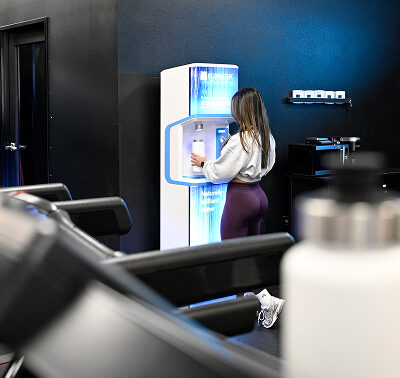 distant shot of woman at gym using flowater refill station